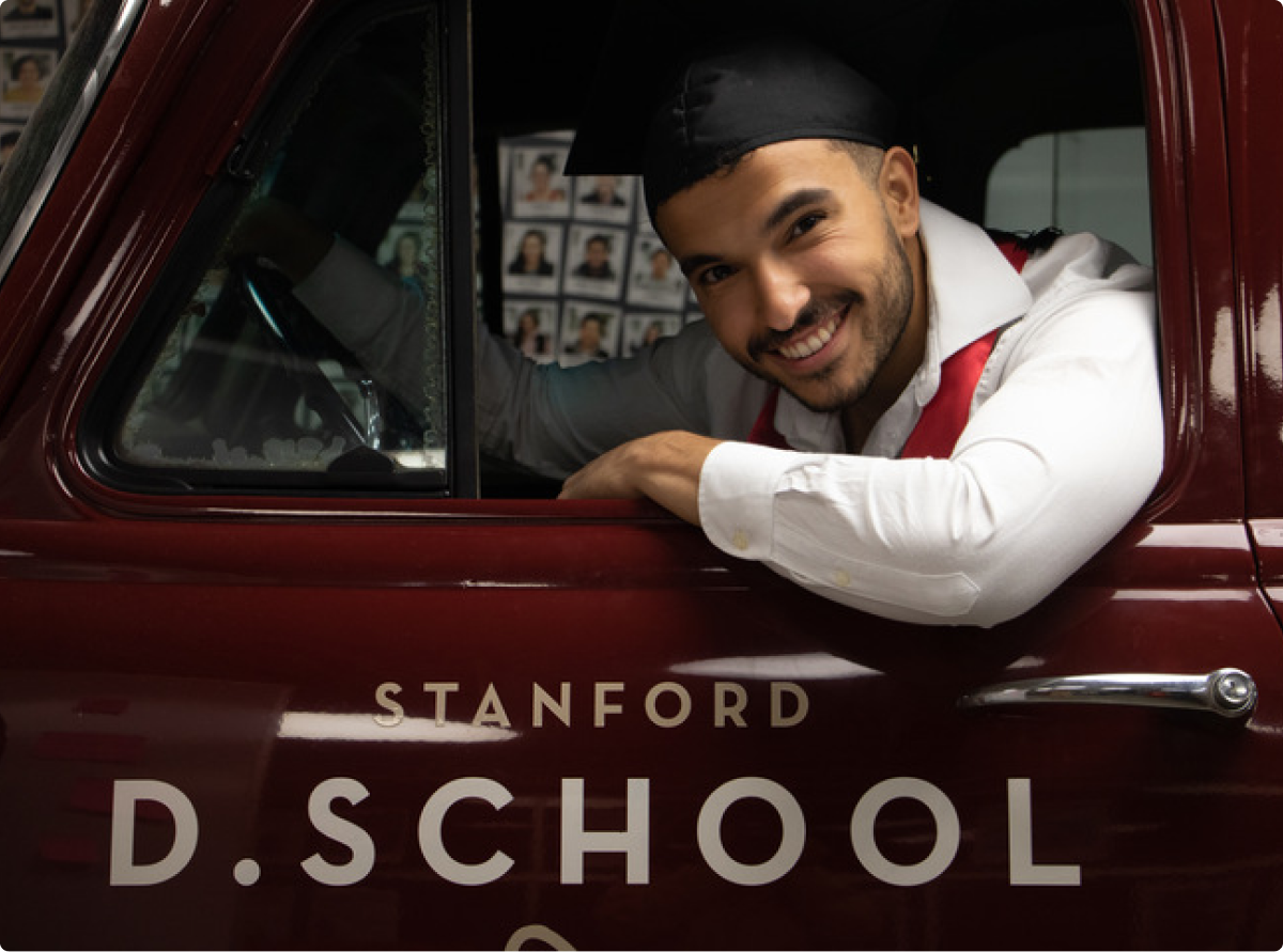 Michael Sezen posing inside the Stanford d.school truck, wearing graduation cap