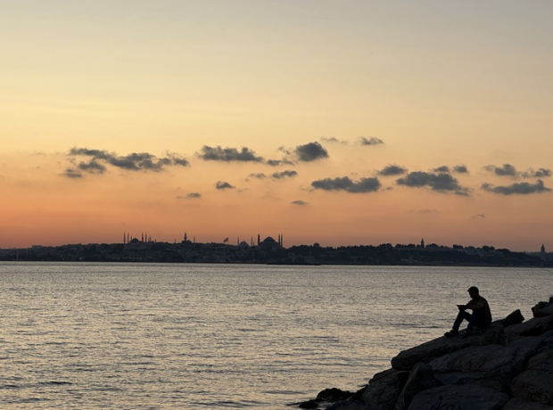Person sitting on river coastline rocks with Istanbul skyline in background