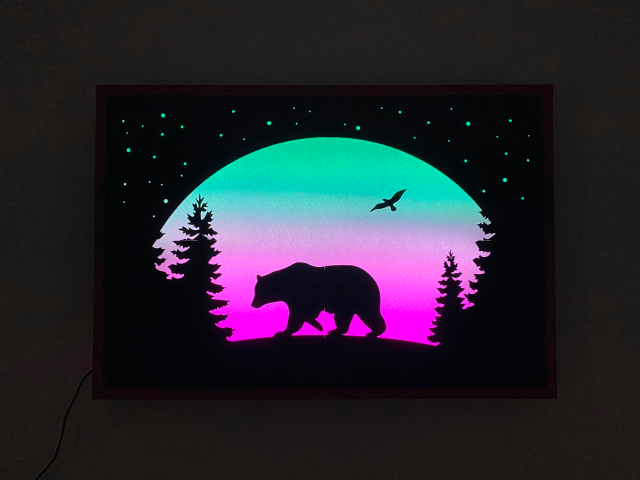 Wall mounted light display with a silhouette of a bear in a forest