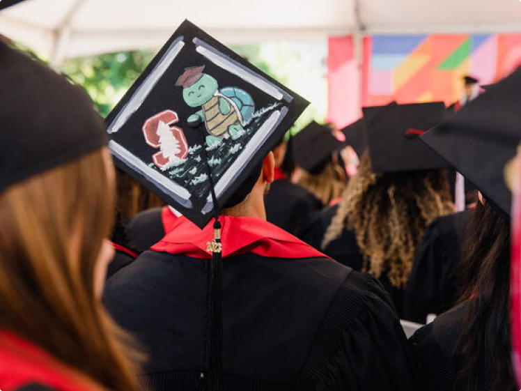Person with back turned sitting with group of graduates with a turtle painted on graduation cap