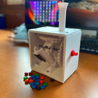 M&M cannon shaped as a box on top of desk with M&Ms scattered in front