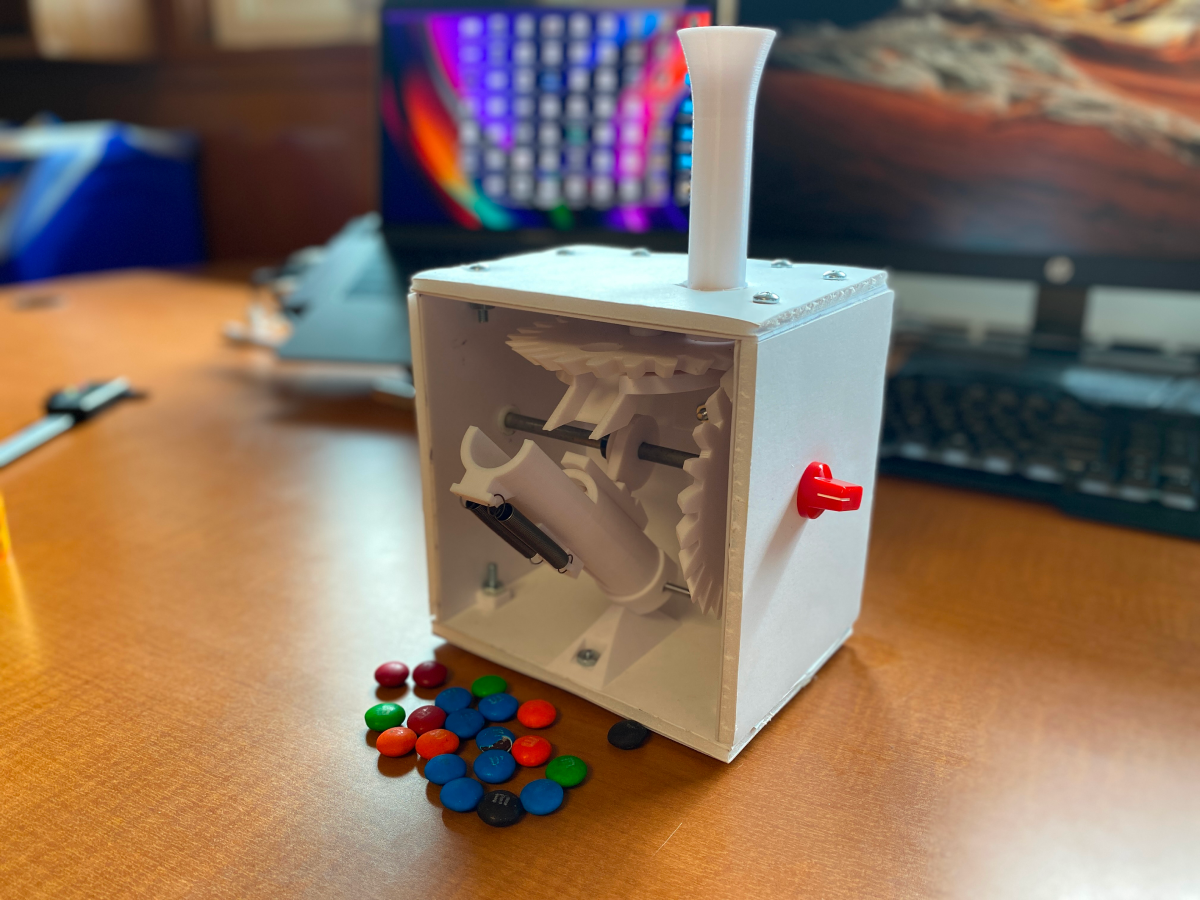M&M cannon shaped as a box on top of desk with M&Ms scattered in front