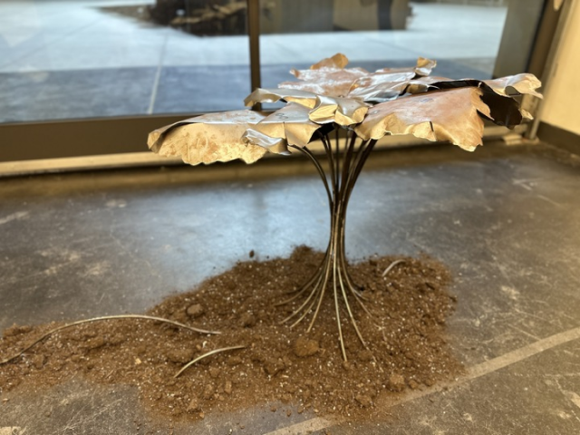 A metal sculpture of a small tree on top of a pile of dirt